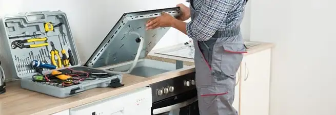Cooktop repair technician lifting a built-in stovetop for service in Dover, DE