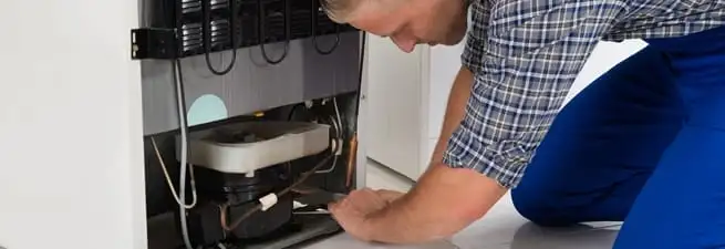 Refrigerator repair technician servicing the compressor and condenser area in Dover, DE
