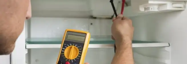 Refrigerator repair technician testing electrical components with a multimeter in Dover, DE